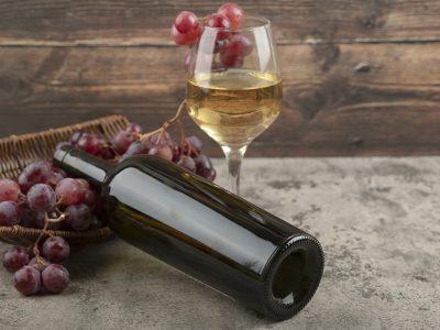 Wicker basket of red grapes with glass of white wine on marble table. High quality photo
